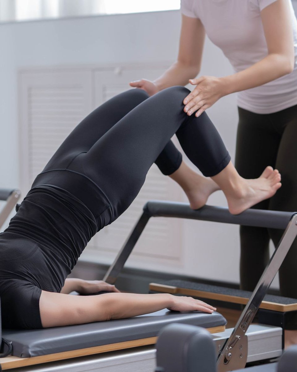 A pilates instructor assisting a client on a reformer